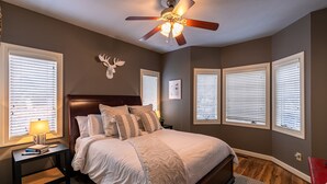 A bedroom with a bed, a nightstand, a lamp, a ceiling fan, and a wall-mounted deer head decoration. - Sugar Shack - Condo with amazing views, close to slopes! (Banner Elk)