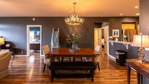 A dining area with a wooden table, chairs, and a chandelier. There is a bench in front of the table, and a trash can is visible to the side. - Sugar Shack - Condo with amazing views, close to slopes! (Banner Elk)