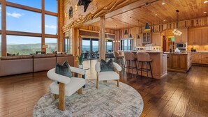 A spacious living area with a large window overlooking a scenic landscape, wooden flooring, and a cozy seating arrangement. - Fine As Wine ~ Resort Pool, Swim-Up Bar, Pickleball, Putt-Putt & Epic Views (Sevierville)