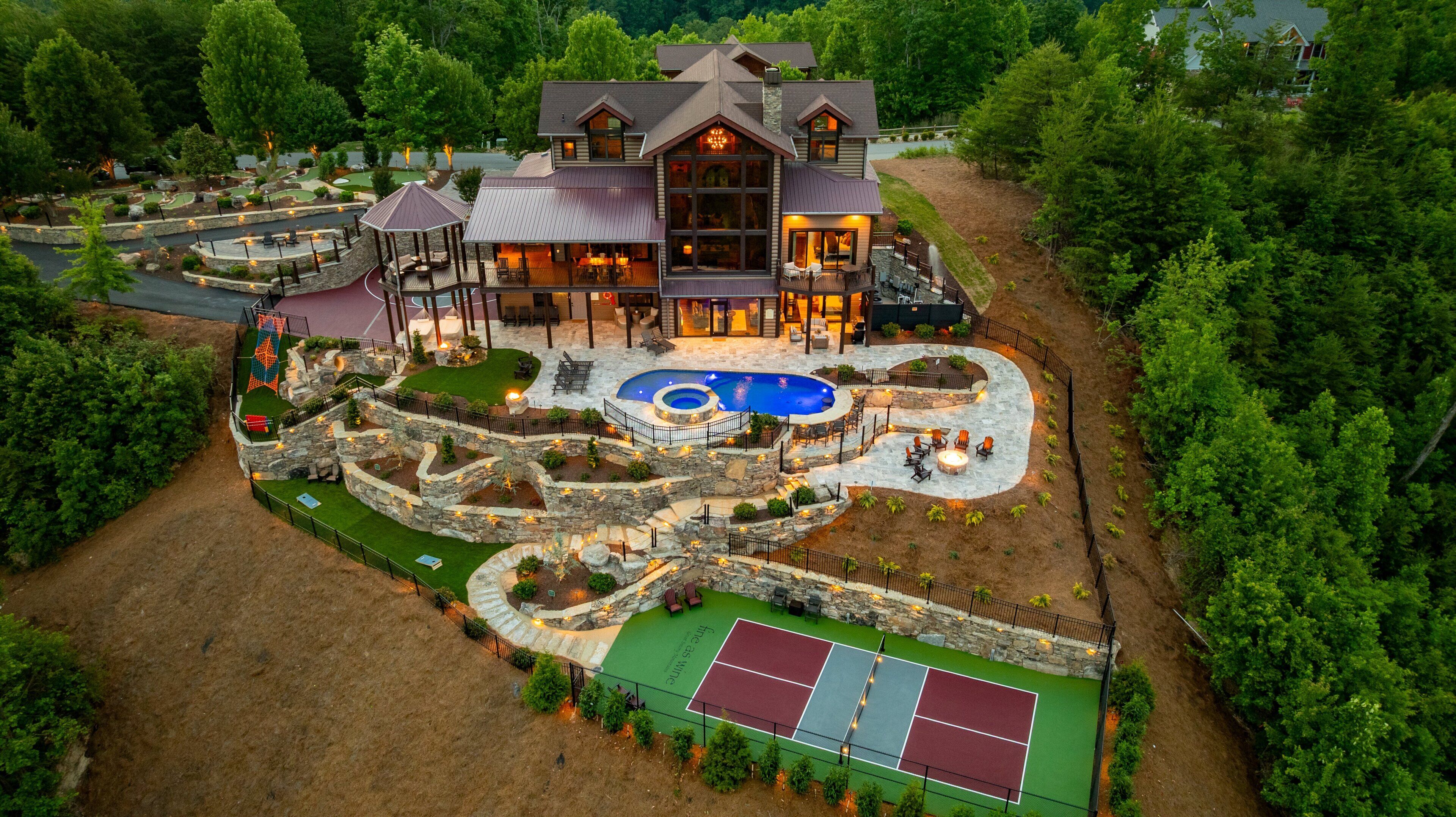 A large house with a swimming pool, tennis court, and patio areas.