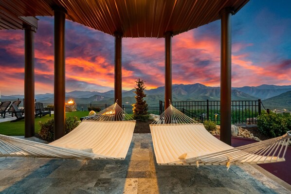A hammock setup under a wooden pergola with a mountain view at sunset.