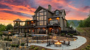 A large, multi-story log cabin with a spacious outdoor patio area featuring a fire pit and outdoor seating. - Fine As Wine ~ Resort Pool, Swim-Up Bar, Pickleball, Putt-Putt & Epic Views (Sevierville)