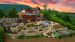 A large, multi-level house with a swimming pool, tennis courts, and a stone retaining wall. - Fine As Wine ~ Resort Pool, Swim-Up Bar, Pickleball, Putt-Putt & Epic Views (Sevierville)