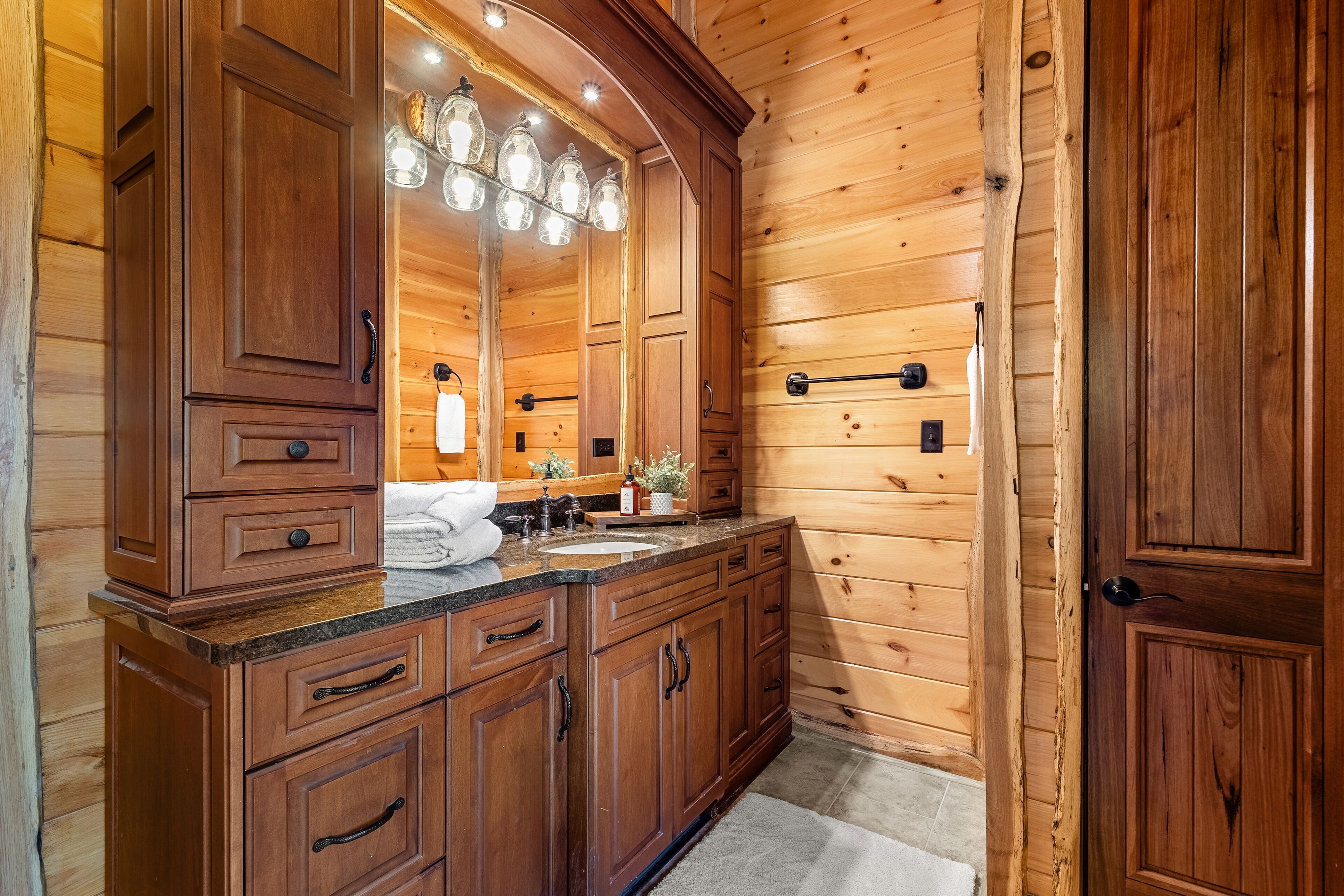 A wooden cabin bathroom with a large vanity, a mirror, and a sink.