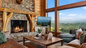 A cozy living room with a stone fireplace, leather furniture, and a large window offering a mountain view. - Fine As Wine ~ Resort Pool, Swim-Up Bar, Pickleball, Putt-Putt & Epic Views (Sevierville)