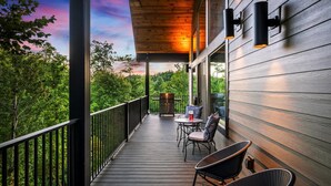 A wooden deck with outdoor furniture, a railing, and a view of trees.