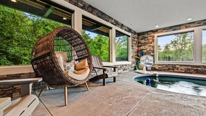 An indoor pool area with a stone wall, large windows, and a wicker chair.