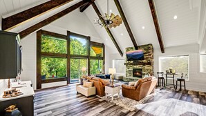 A spacious living room with a high ceiling, large windows, a fireplace, and a dining area.