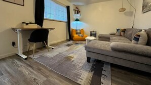 A living room with a gray sofa, a small table, a desk with a chair, a ceiling fan, and a window with blinds. - Private 1 bed/1bath by Downtown Columbus, Arenas, & Hospitals (Columbus)