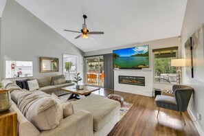 A modern living room with a sofa, coffee table, fireplace, TV, and a ceiling fan.