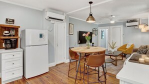 Una cucina moderna con elettrodomestici bianchi, un'area pranzo con un tavolo rotondo e sedie, e un soggiorno con divano e televisore.