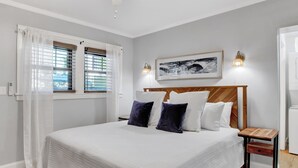 Ein ordentlich eingerichtetes Schlafzimmer mit einem großen Bett, zwei Nachttischen, einer Wandleuchte und einem gerahmten Bild über dem Bett.