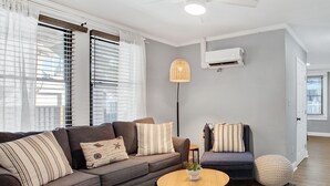 Ein modernes Wohnzimmer mit einem grauen Sofa, gestreiften Kissen, einem runden Couchtisch aus Holz und einem Blumentopf.