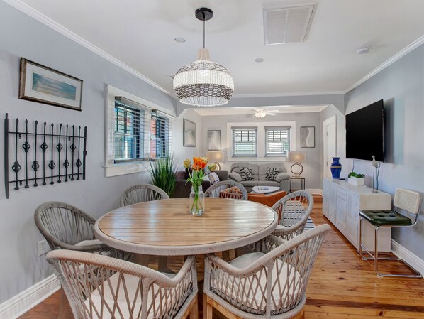 A dining area with wicker chairs, a wooden table, and a chandelier. - Entire Unit Steps from the Beach | Heated Pool Access (Tybee Island)