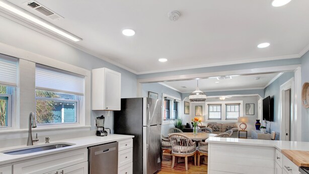 Una cocina moderna con armarios blancos, un refrigerador de acero inoxidable y una mesa de comedor de madera con sillas.