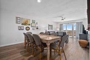 A dining area with a wooden table and wicker chairs, a ceiling fan, and a view of the outdoors through large windows. - La Mirage Condo 236 Beachfront Resort Condominiums with Private Boardwalk (Port Aransas)
