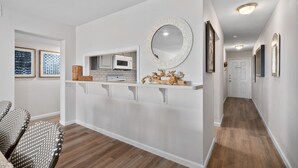 Un pasillo con pared blanca, microondas, un espejo decorativo y una puerta al final.