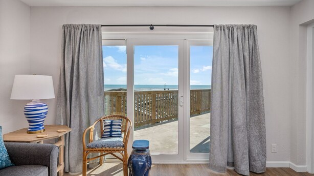 Una habitación con vista a la playa, una silla de mimbre, una mesa con una lámpara y un jarrón azul.