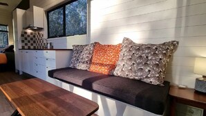 A compact kitchen with a bench seating area, a wooden table, and a window with a view of trees. - Tiny House/Retreat in Adelaide Hills. Secluded, peaceful, country views. (Macclesfield)