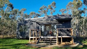 A rustic wooden cabin with a covered porch and a small deck, surrounded by trees. - Tiny House/Retreat in Adelaide Hills. Secluded, peaceful, country views. (Macclesfield)