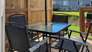 An outdoor patio with a glass table and four chairs, a wooden fence, and a house in the background. - Stylish Vacation Home (Dieppe)