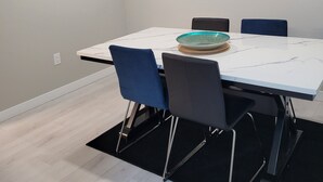 A modern dining area with a white table, blue chairs, and a glass bowl centerpiece. - Stylish Vacation Home (Dieppe)