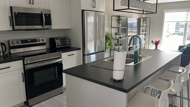 A modern kitchen with stainless steel appliances, a central island with seating, and a view of the outside. - Stylish Vacation Home (Dieppe)