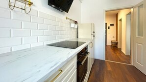 Une cuisine avec des carreaux de céramique blancs disposés en motif métro, un téléviseur noir fixé au mur au-dessus du comptoir et un plancher en bois.