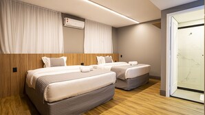 A hotel room with two beds, wooden paneling, a large window, and an air conditioning unit.