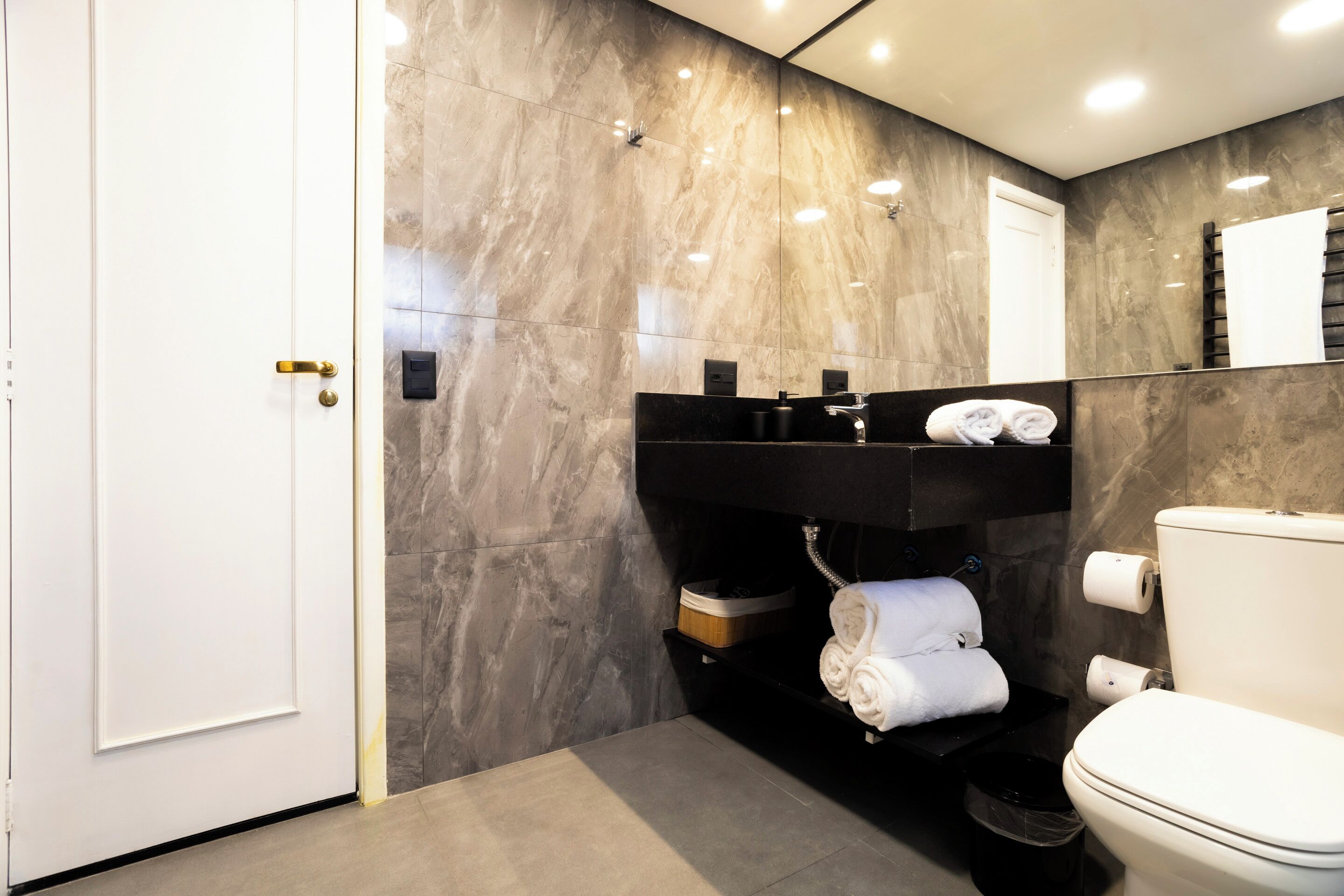 Een moderne badkamer met een marmeren wand, een zwarte wastafel en een toilet.