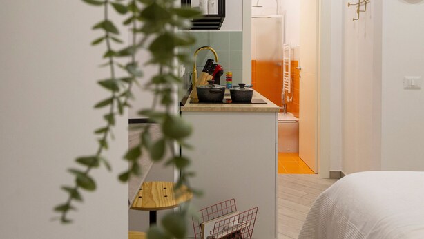 A modern kitchen with a sink, stove, and cabinets, a small dining area with a table and chairs, and a bedroom with a bed and a nightstand. - Lovely and tiny unit in the City center (Trieste)