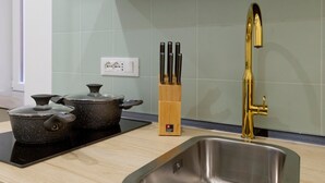A kitchen with a stainless steel sink, two pots on an induction cooktop, a knife block, and a gold faucet. - Lovely and tiny unit in the City center (Trieste)