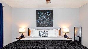 Habitación de hotel con una cama grande, dos lámparas de noche, un cuadro abstracto negro y un espejo en la pared.