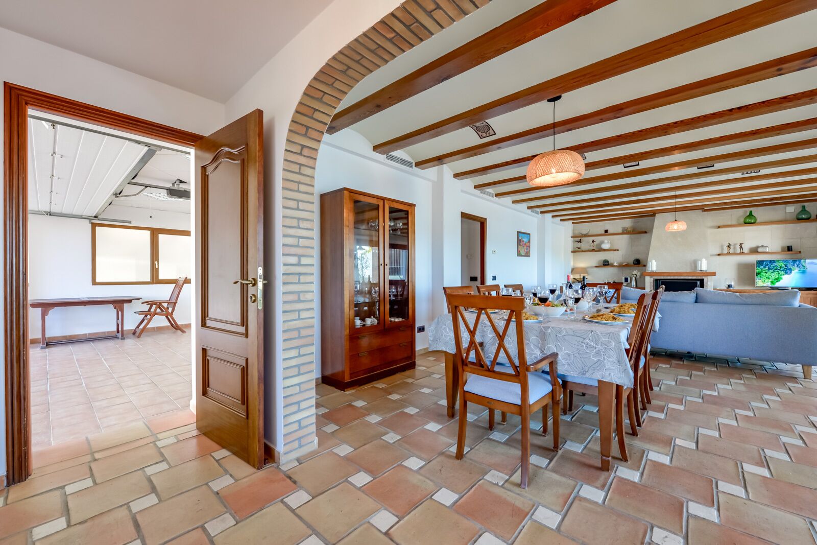 A spacious dining area with a large wooden table and chairs, a kitchen with a TV, and a view of the outdoors.