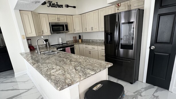 A modern kitchen with a granite countertop, stainless steel appliances, and a black trash bin. - Lux Home, Laplace (LaPlace)