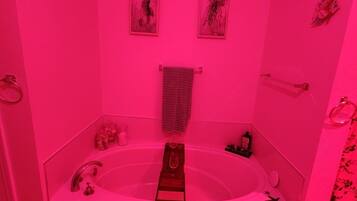 A bathroom with a large bathtub, a glass shower enclosure, and a pink color scheme.