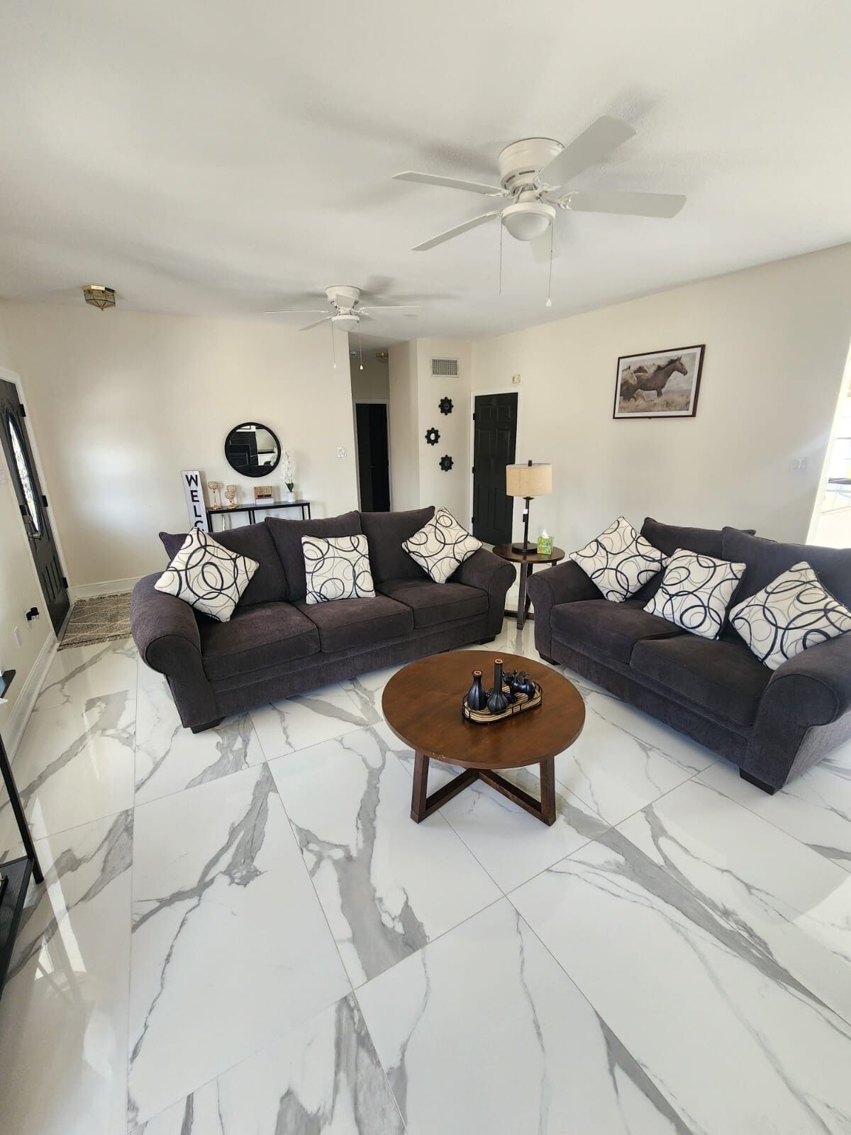 A living room with a dark brown sectional sofa, a round coffee table, and a ceiling fan.