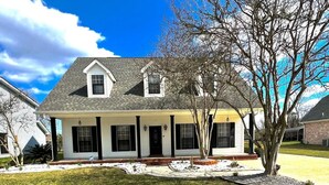 A two-story house with a front porch, a small garden, and a tree in the yard. - Lux Home, Laplace (LaPlace)