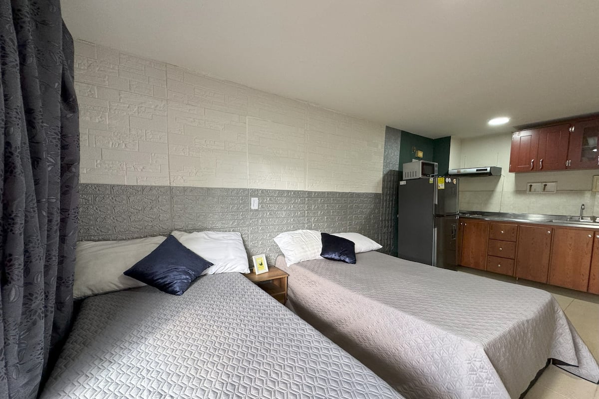 A room with two beds, a kitchenette, and a brick-patterned wall.