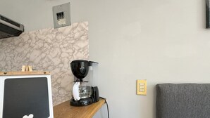 Une petite cuisine équipée d’une machine à café, d’un tableau noir et d’un canapé gris.