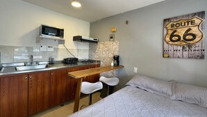 Une cuisine compacte équipée d’un four à micro-ondes, d’une cuisinière et d’un évier. On y trouve un lit avec une couverture matelassée et des oreillers. Un panneau indiquant la Route 66 est accroché au mur.