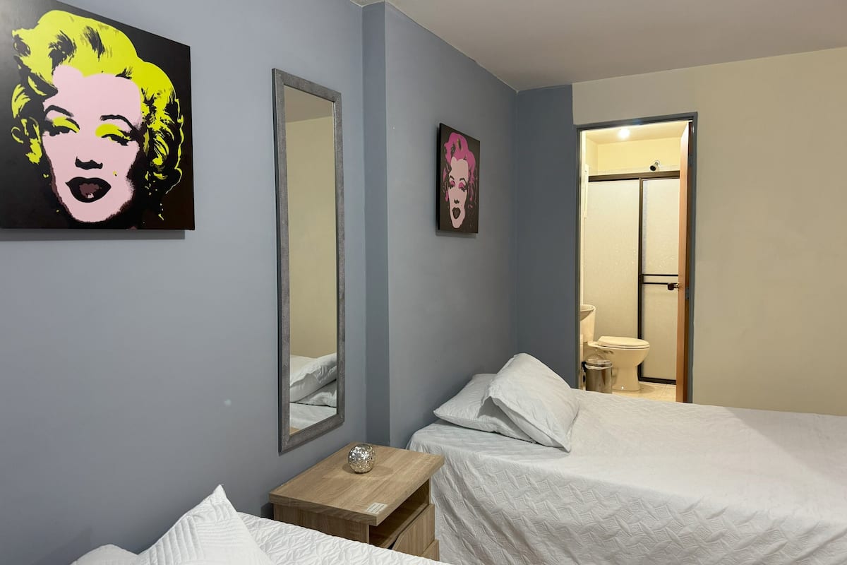 A bedroom with two beds, a wooden nightstand, and two wall-mounted mirrors.