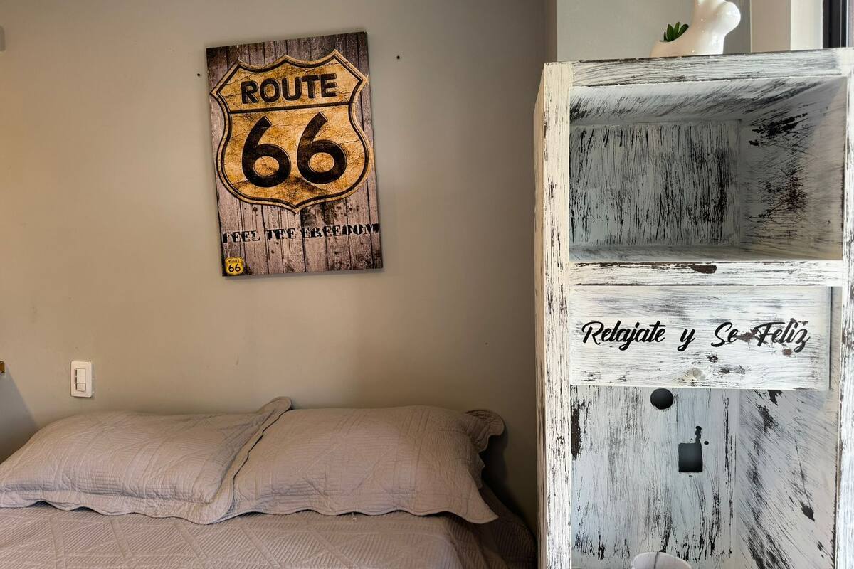 A bedroom with a bed, a Route 66 sign, and a white dresser with a distressed finish.