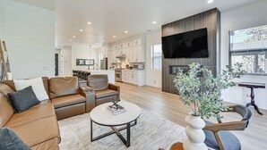 A modern living room with a brown leather sofa, a round coffee table, and a flat-screen TV mounted on the wall. - New Modern House Built in 2024.  5 Beds and 3.5 Baths. 3020 SQFT (Flagstaff)