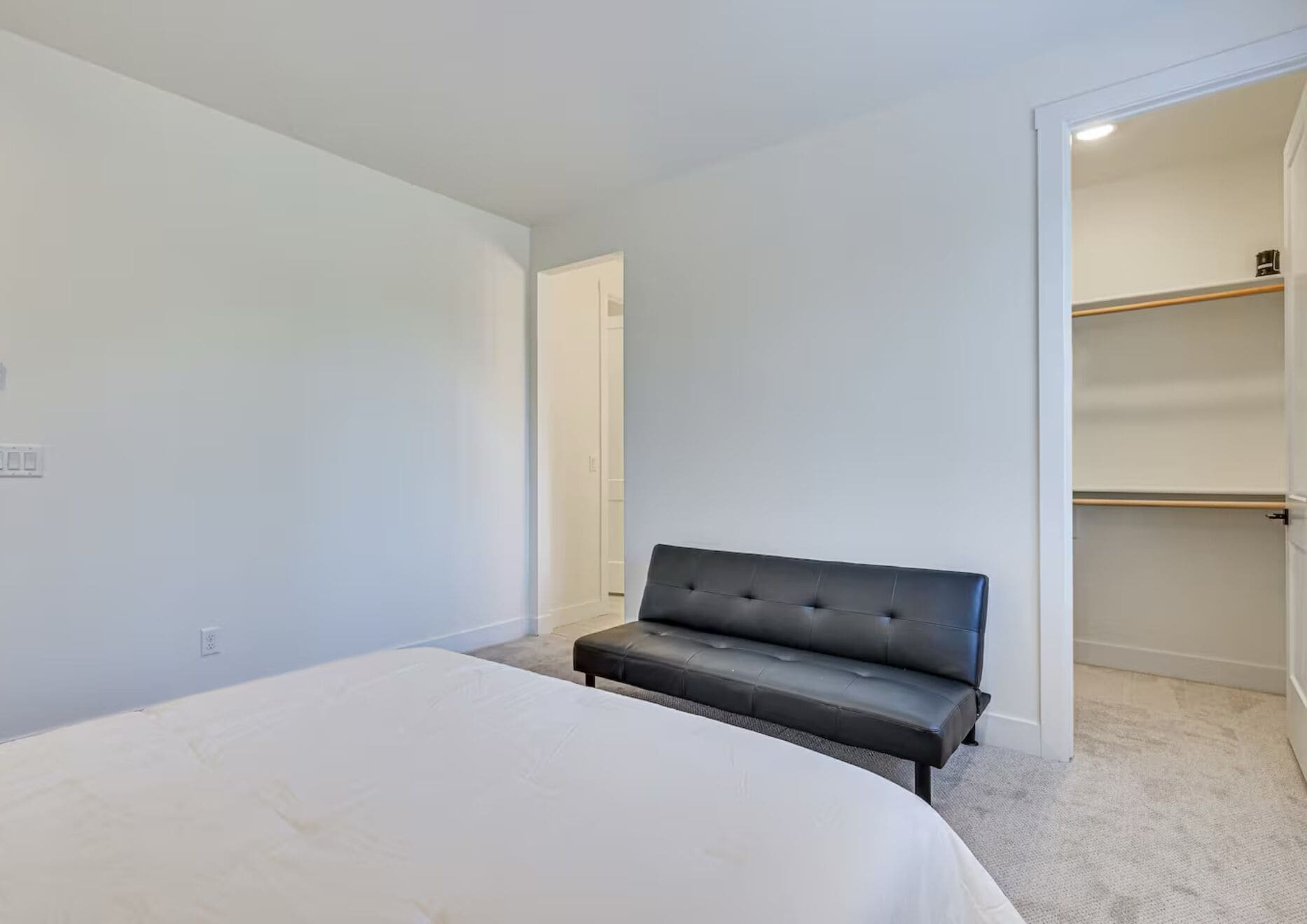 A bedroom with a bed, a black sofa, and a walk-in closet.