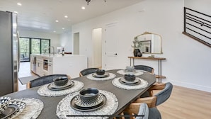 A modern kitchen with a central island, a dining area with a dark table and woven placemats, and a large mirror above a console table. - New Modern House Built in 2024.  5 Beds and 3.5 Baths. 3020 SQFT (Flagstaff)