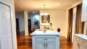 A modern kitchen with a central island, wooden flooring, and white cabinetry. - Macon a Little Music House.  Family-sized Home <1 Mile to Mercer & Downtown (Macon)