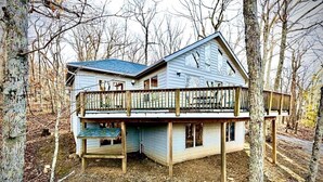 Eine zweigeschossige Holzhütte mit Balkon, umgeben von Bäumen.