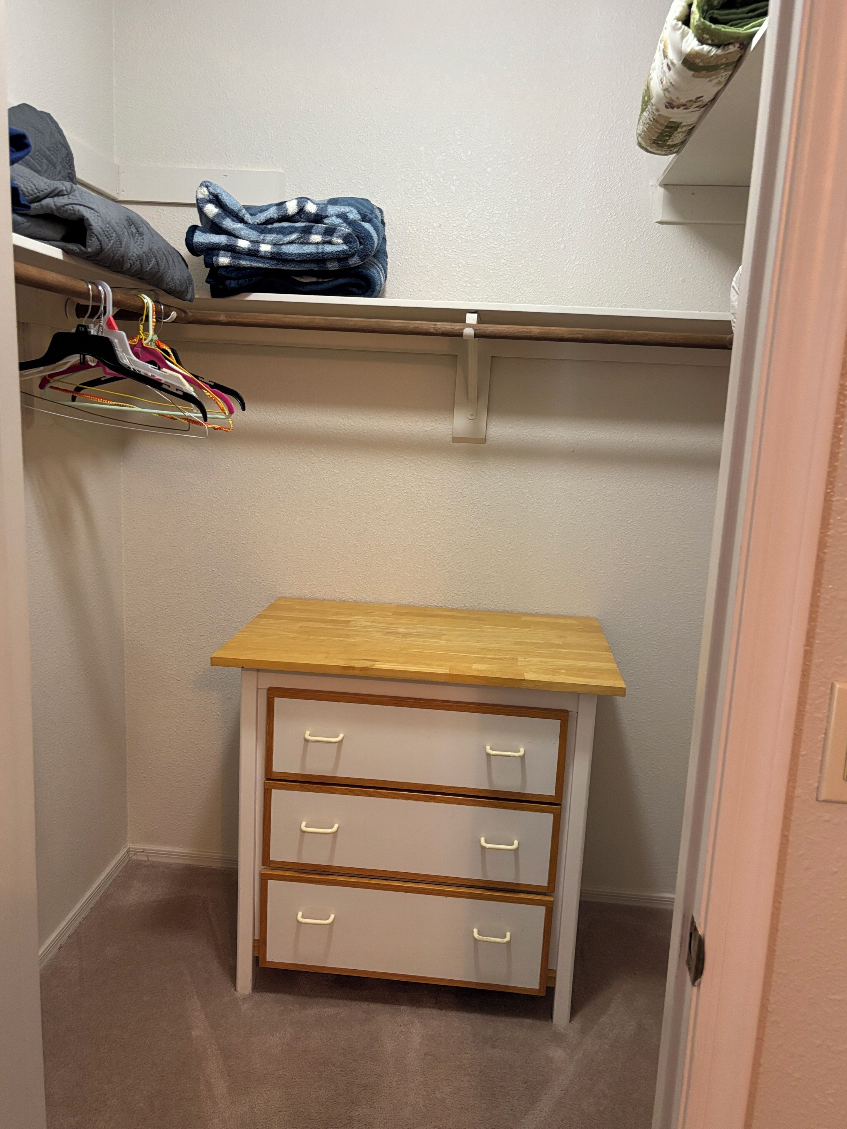 A small wooden dresser with three drawers and a shelf above it in a closet.