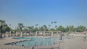 Piscina com várias pistas, rodeada por palmeiras e áreas sombreadas.